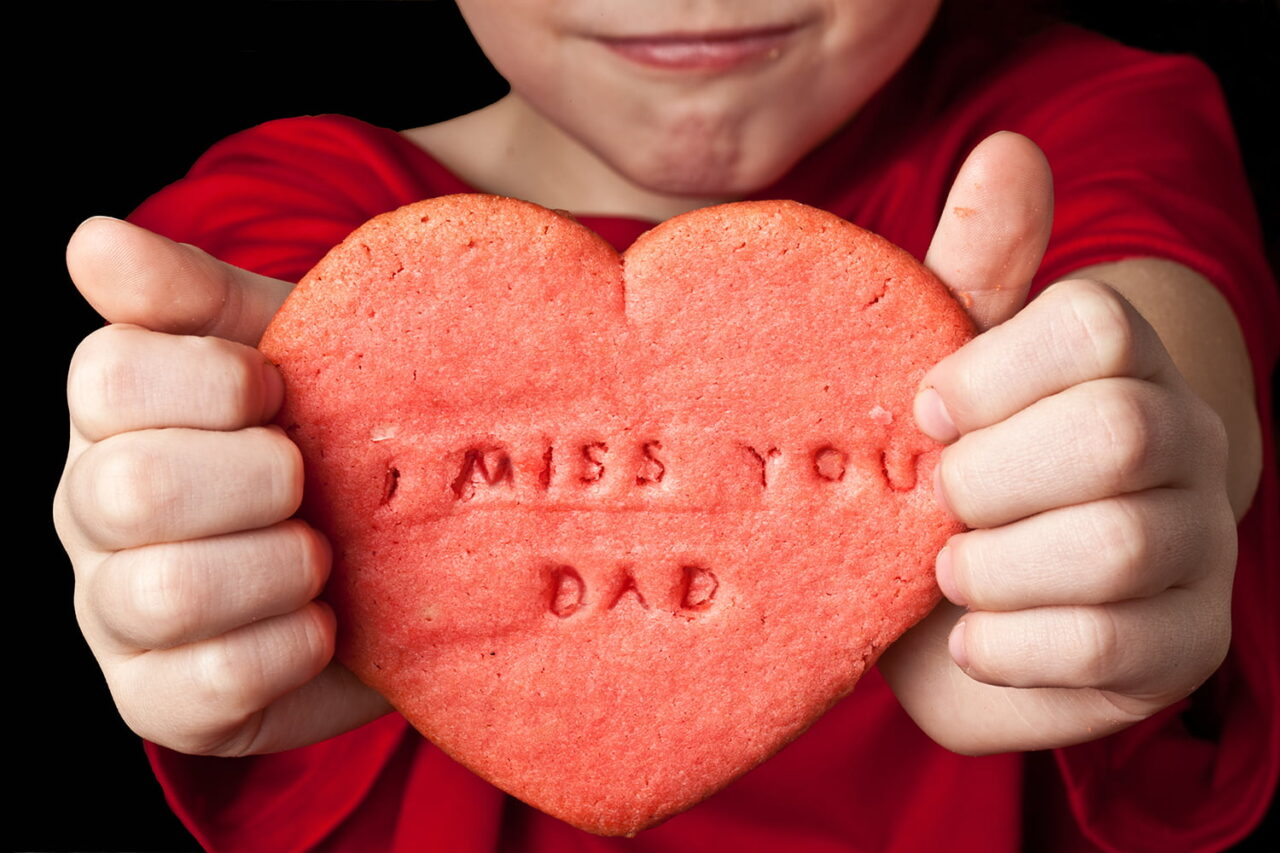 Young child holding a cookie with a message I miss you dad